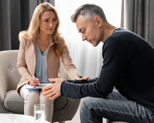 Terapeuta pocieszająca zasmuconego mężczyznę, kładzie dłoń na jego dłoniach w geście wsparcia.